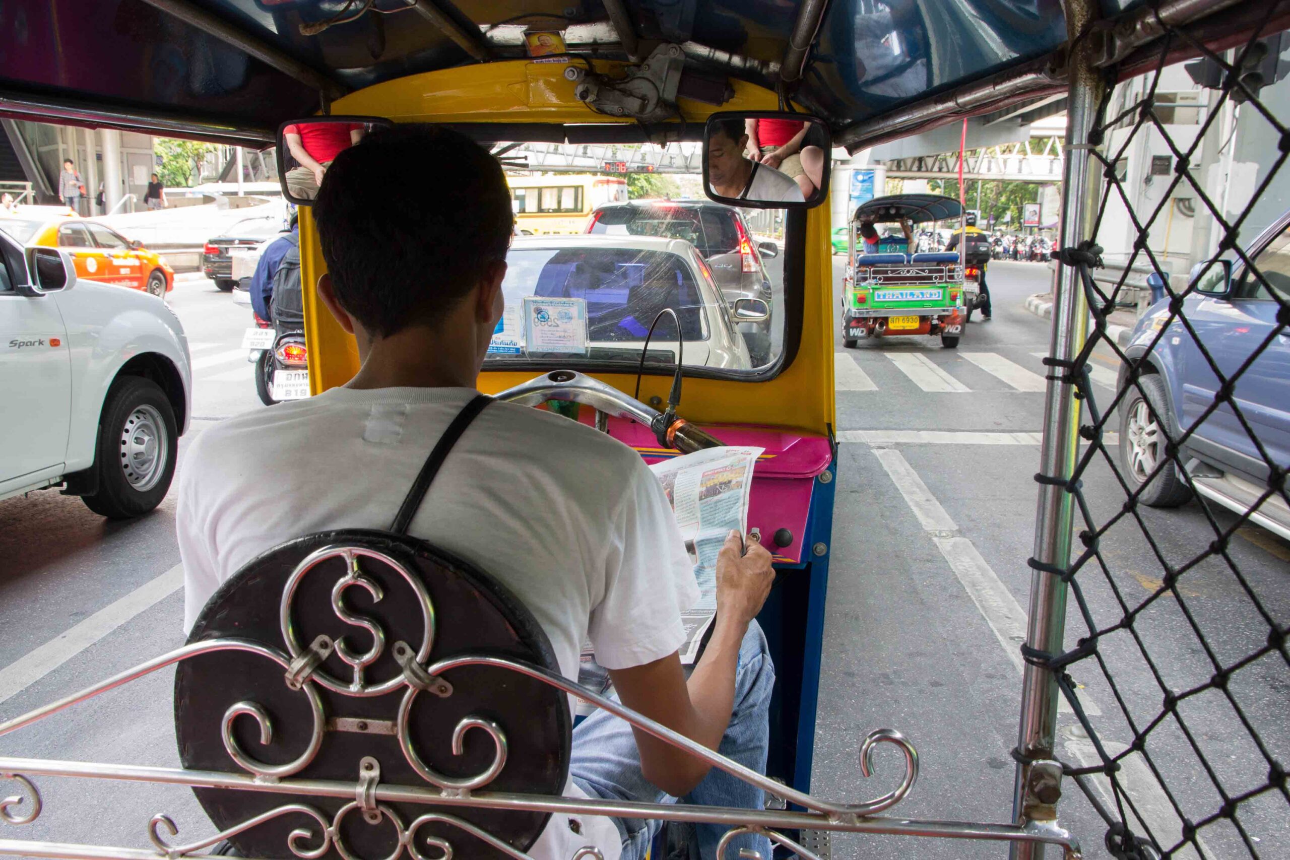Tuk-tuk driver reading a newspaper while stopped in traffic in Bangkok